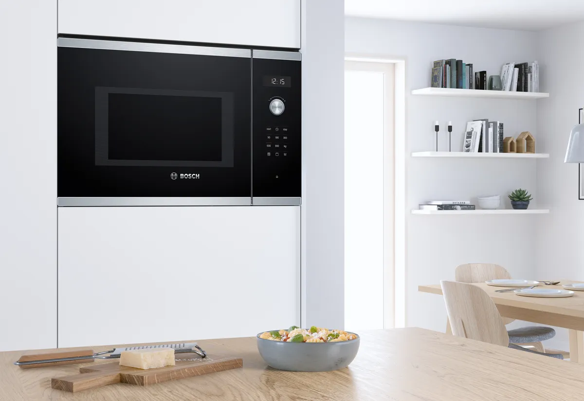 A plate of pasta on top of the table near a microwave.