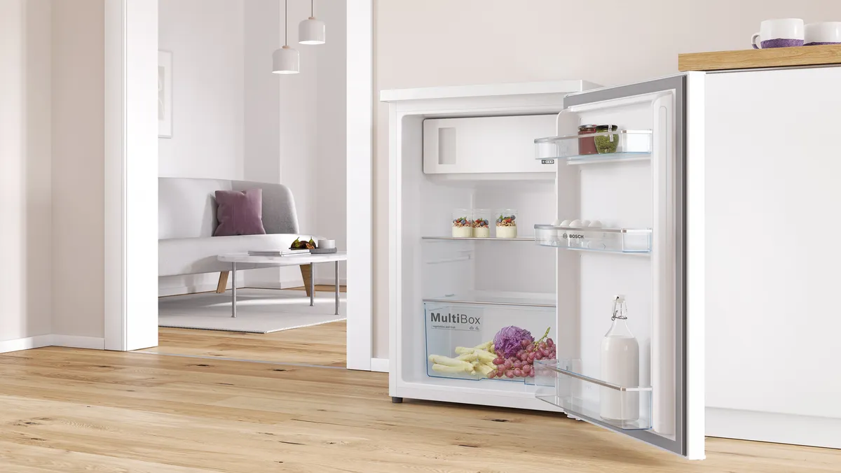 Mini ledusskapja durvis ir atvērtas, atklājot saldētavas nodalījumu un noliktavas plauktus.