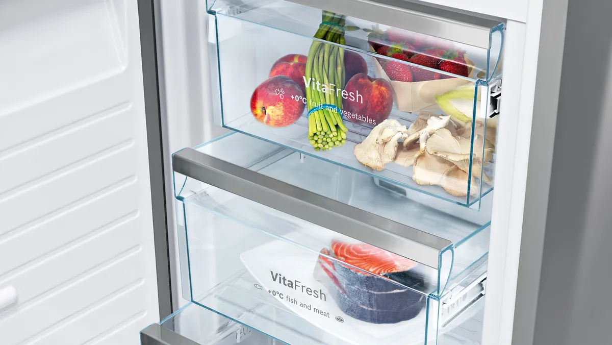 Atidarytas šaldytuvas su „VitaFresh“ stalčiais, kurių vienas užpildytas šviežiomis daržovėmis, o kitas – šviežia žuvimi.