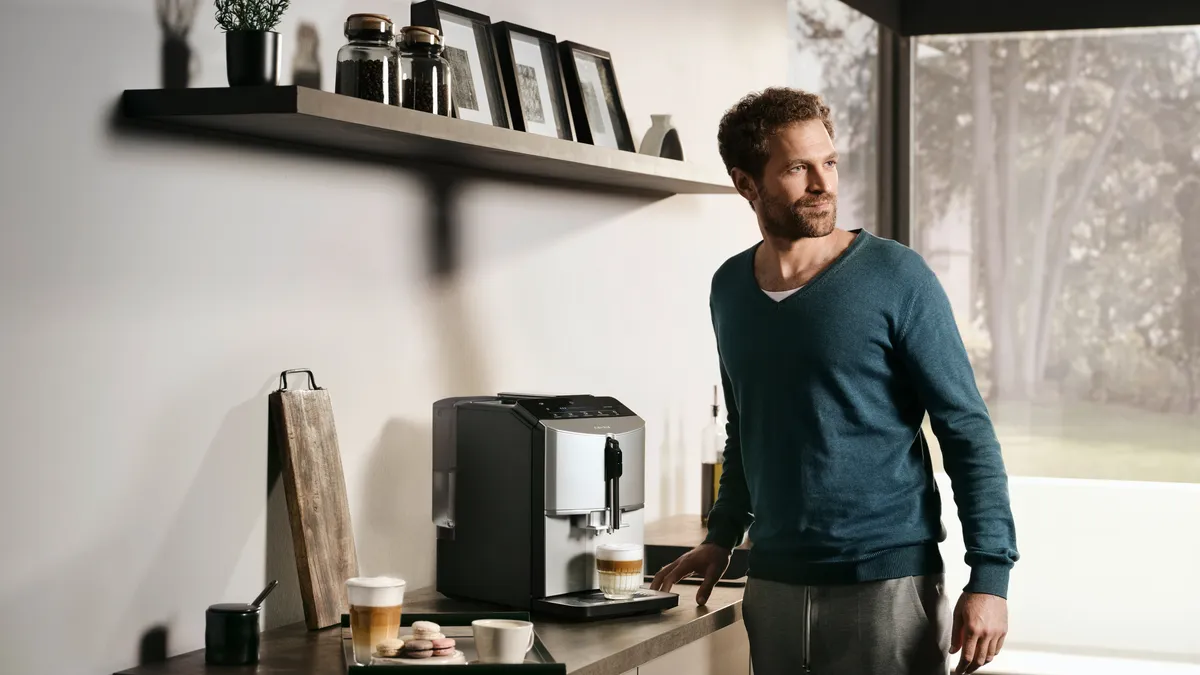 GuMan standing at a kitchen counter, preparing a cappuccino with the EQ300 fully automatic espresso machine.