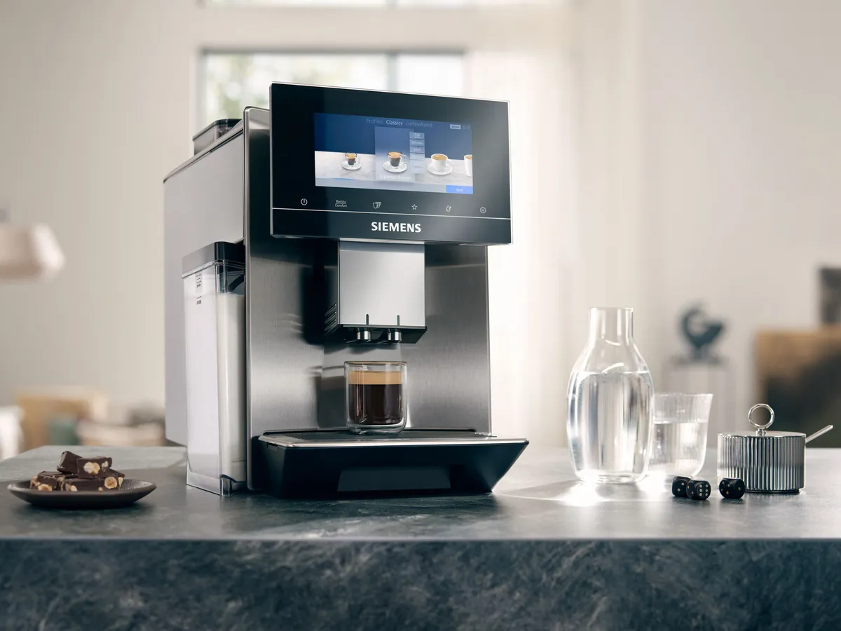 EQ900 fully automatic espresso machine stands on a granite work top, next to it a water carafe with glass, pastries on a small plate  and a sugar bowl.