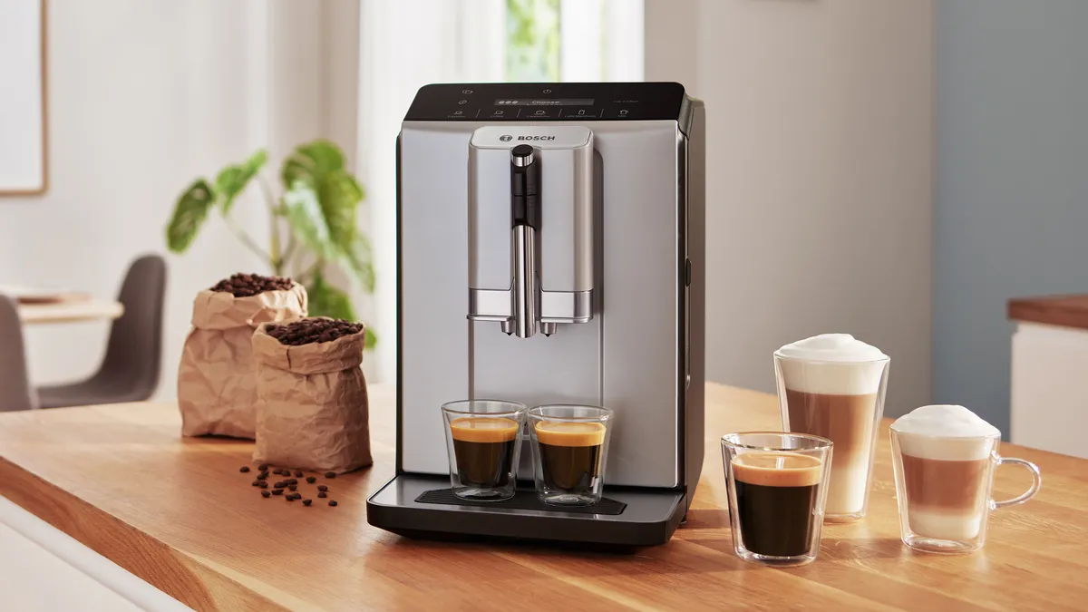 Espressor de cafea complet automat VeroCafe Series 8, alături de 3 căni cu diferite stiluri de cafea, pe blatul de bucătărie.