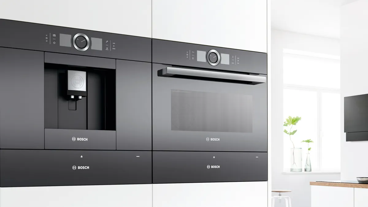 Built-in coffee machine next to built-in oven in a white interior kitchen.