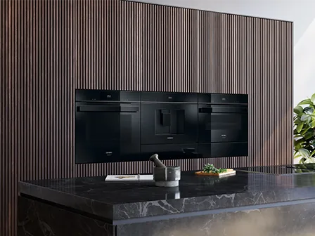 Modern kitchen with dark wood paneling, black appliances, and a marble countertop.