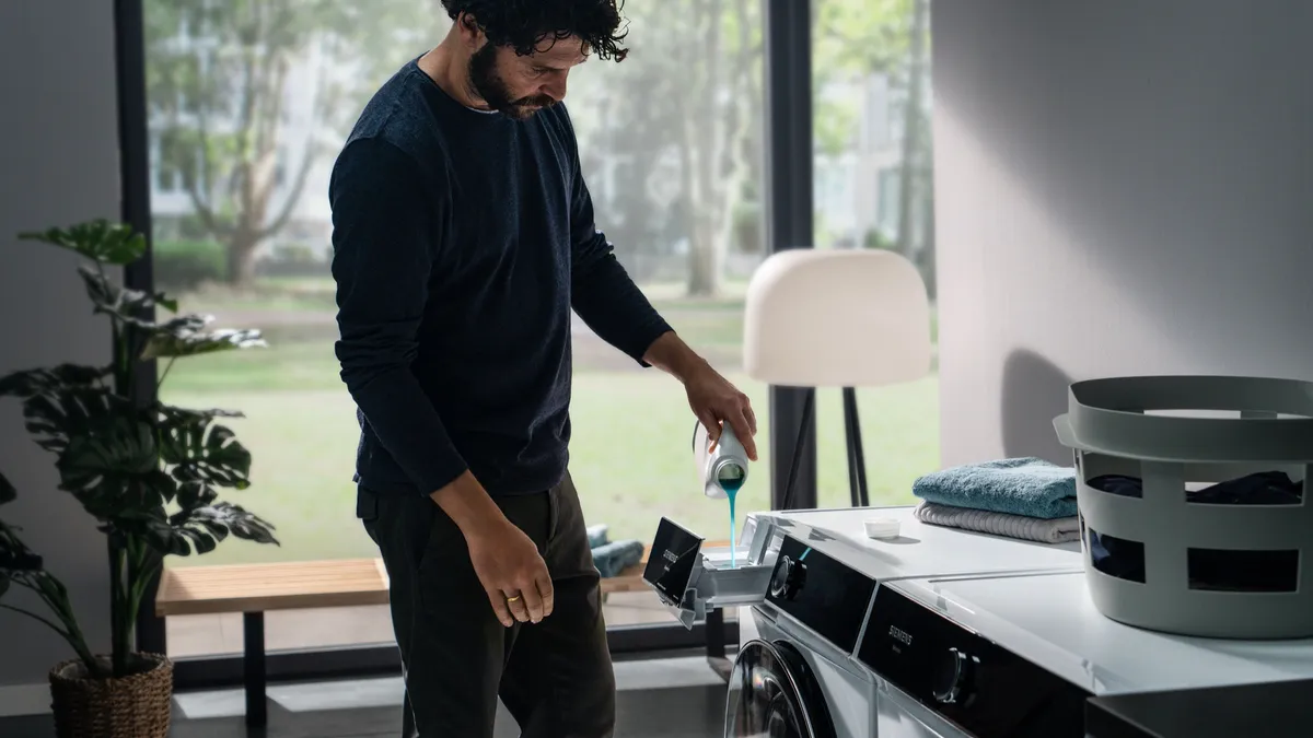 Siyah gömlekli adam bitkiler ve mobilyalarla odada duruyor.