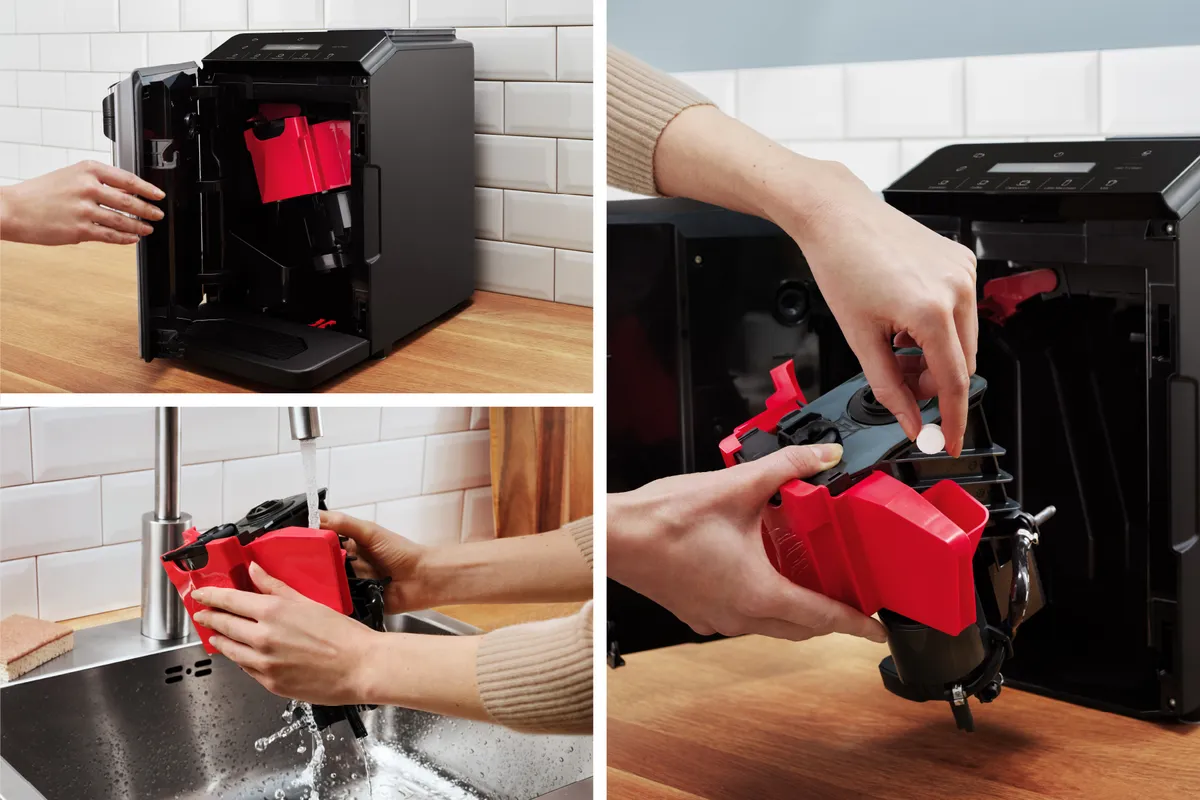 Hands removing a red component from a black appliance, rinsing it under running water at a sink.