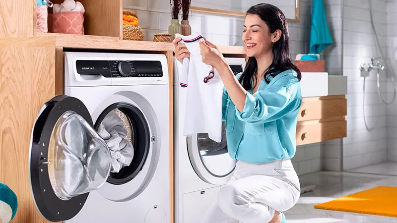 Kadın elbiseleri ev çamaşır odasında yıkama makinesine yükler.