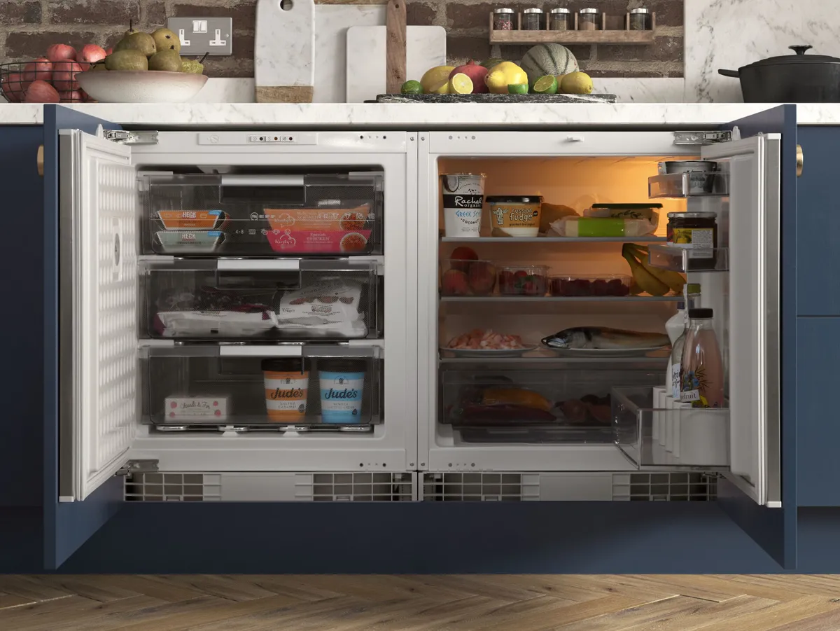 Offener Kühlschrank mit geordneten Regalen, in denen verschiedene Lebensmittel vor einem modernen Küchenhintergrund ausgestellt sind.