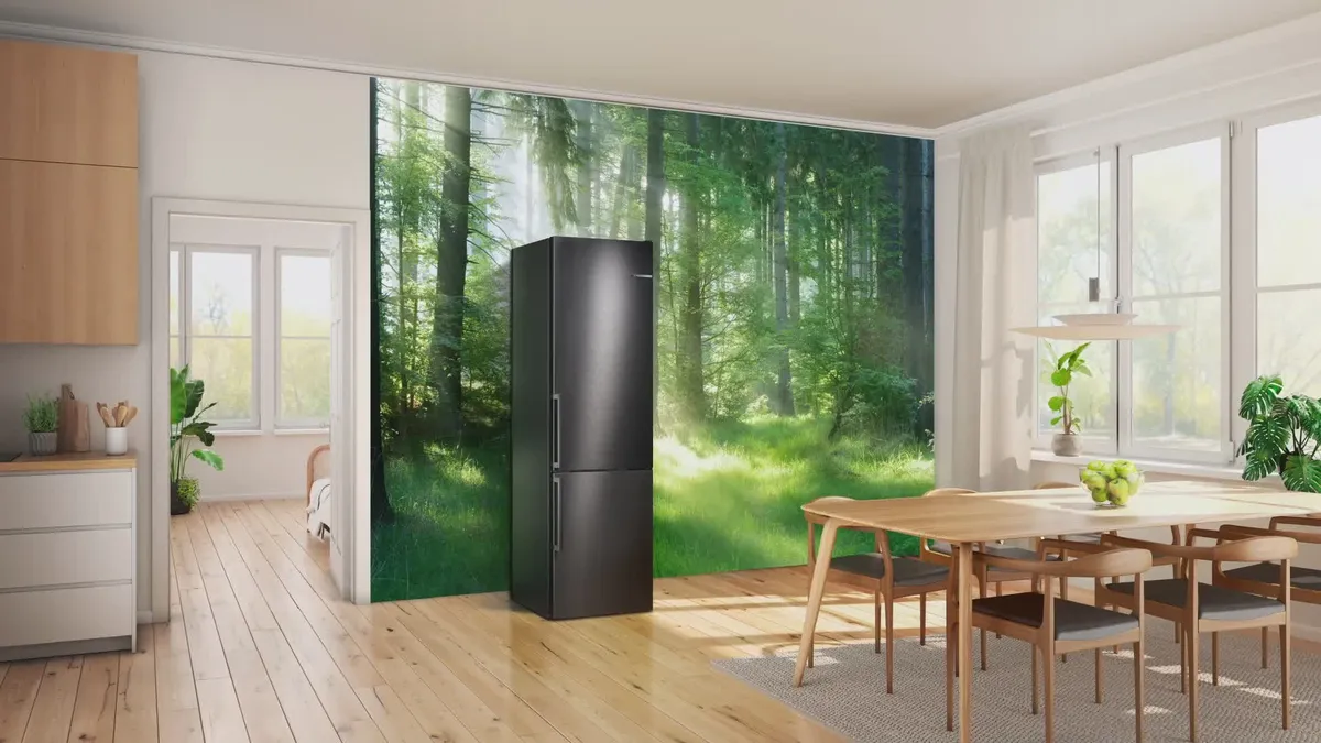 Cuisine moderne avec parquet, réfrigérateur noir et fresque murale représentant une forêt luxuriante, éclairée par la lumière naturelle.
