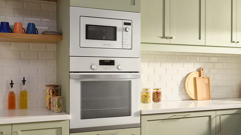 Beyaz kabinlerle modern mutfak, mikrodalga, fırın ve raflarda yemek aletleri.