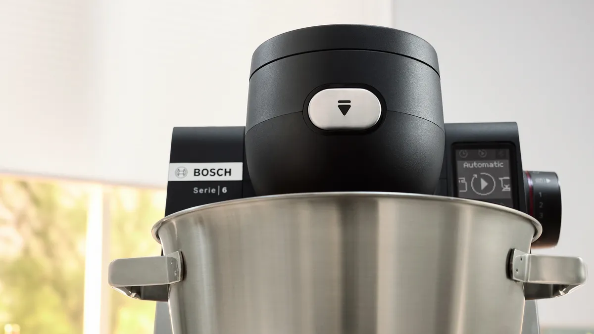 Close-up van een Bosch Serie 6-keukenmixer, met een zwarte bovenkant en een bedieningsknop boven een glanzende roestvrijstalen kom.
