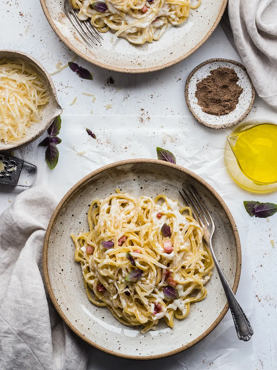 Een prachtig opgediende spaghetti met kaas en verse kruiden, omringd door ingrediënten zoals olijfolie en specerijen.