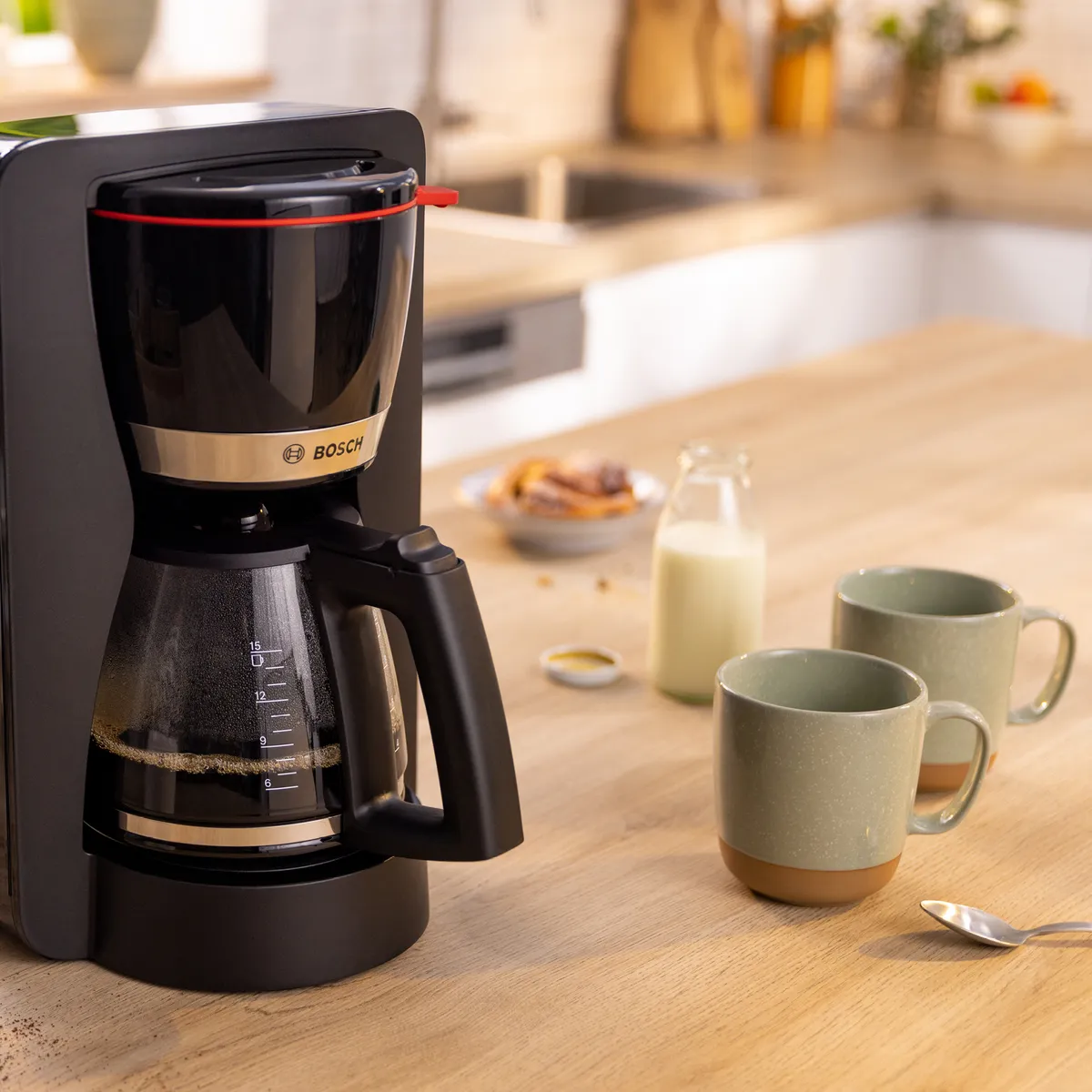 Filter coffee machine with carafe of coffee next to cups on kitchen counter.