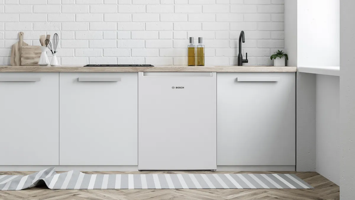 A mini fridge is positioned between white cabinets beneath a kitchen counter.