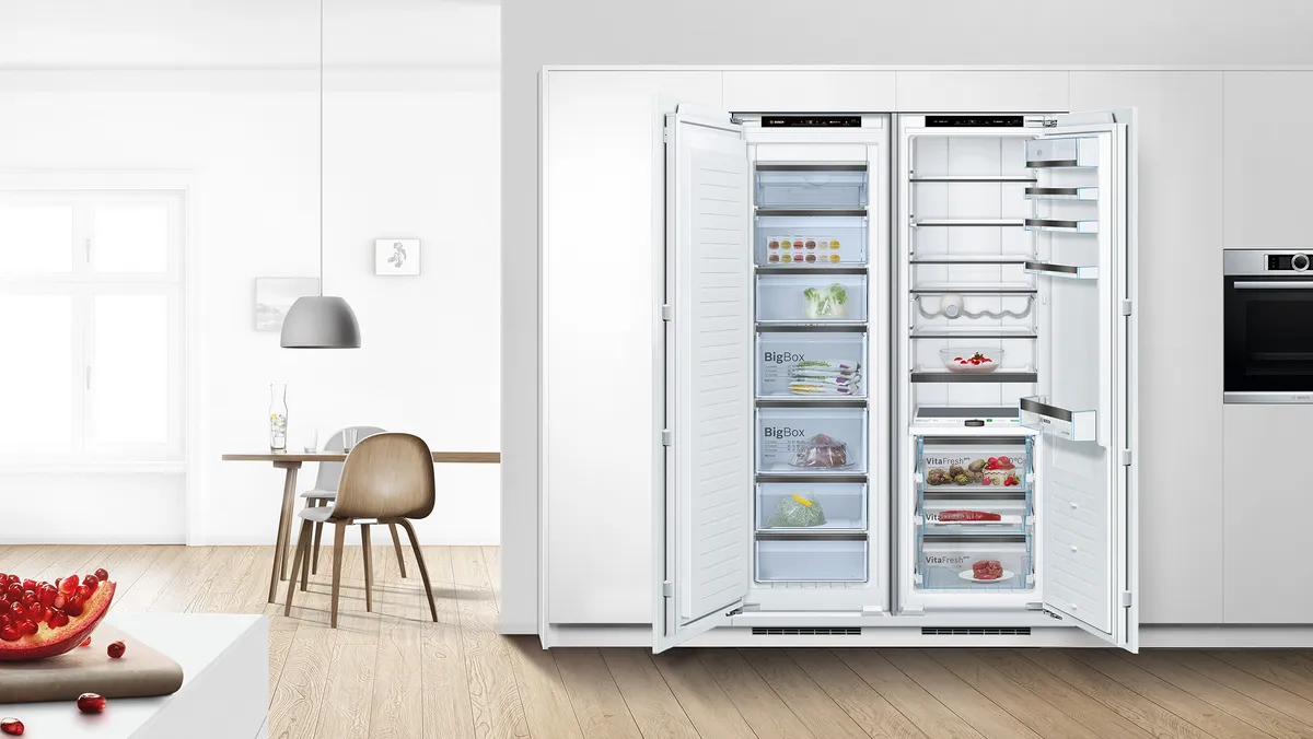 Atvērta iebūvēta saldētava blakus atvērtam iebūvētam ledusskapim.