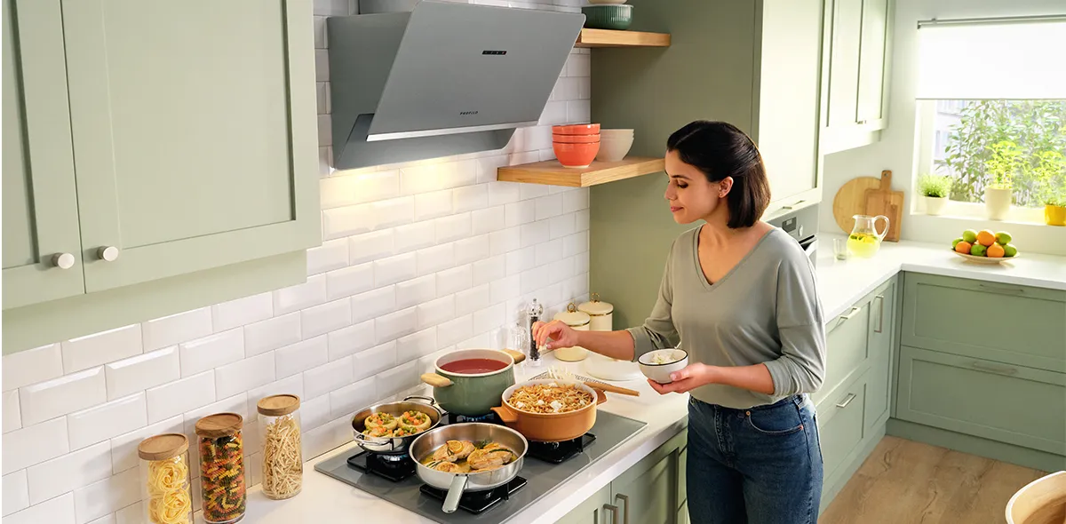 Kadın çeşitli yemekler ve aletlerle modern bir mutfakta yemek pişiriyor.