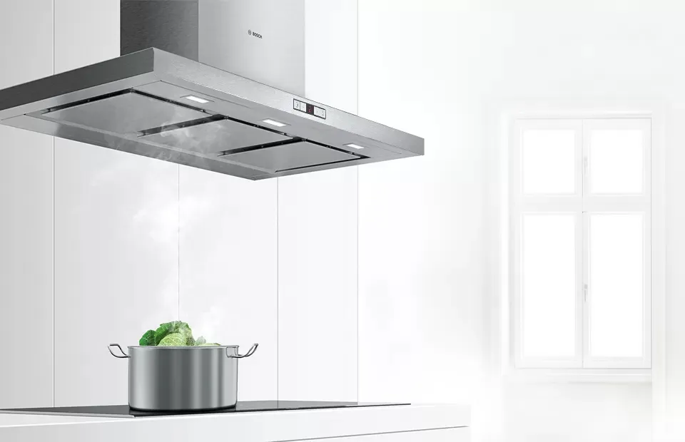 Modern kitchen featuring a stylish hood above a wooden island, with a pot and fruit bowl.