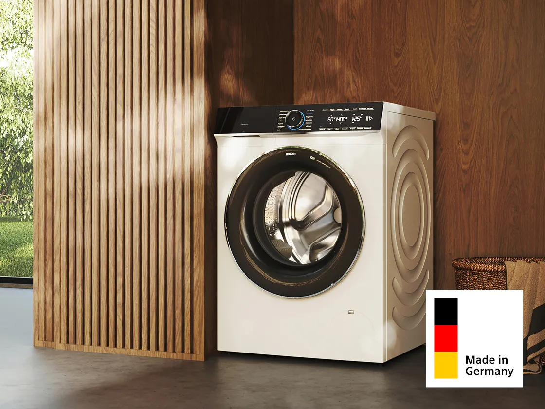 Eine moderne weiße Waschmaschine steht an einer Holzwand. In der Ecke prangt ein „Made in Germany“-Etikett.