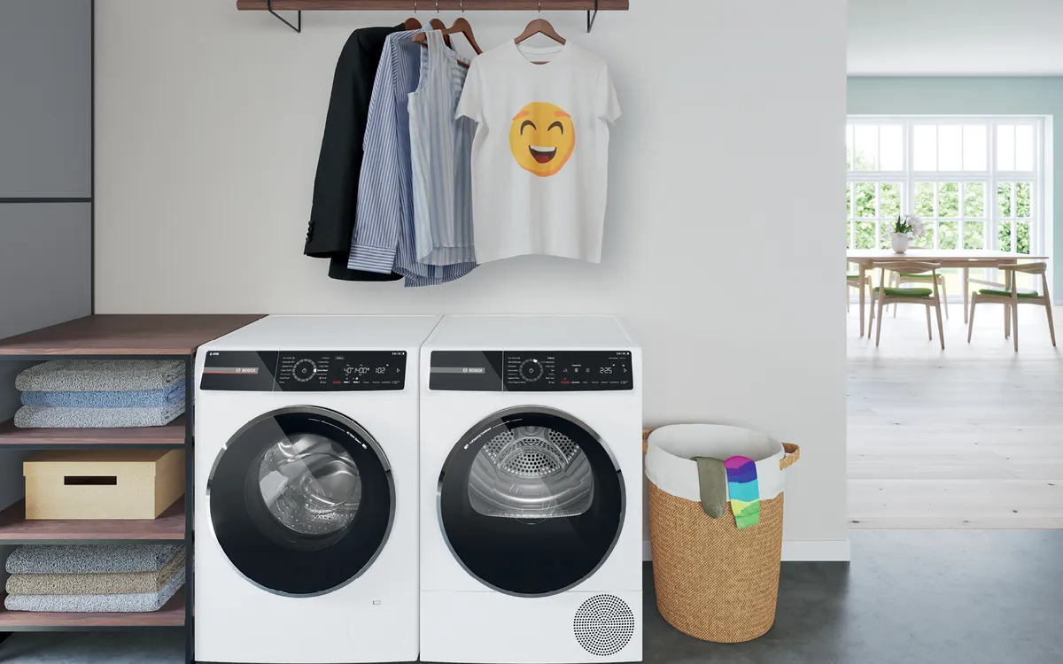 Een moderne wasruimte met gestapelde wasmachine en droogkast, hangende kleren en een rieten mand met kleurrijke sokken.