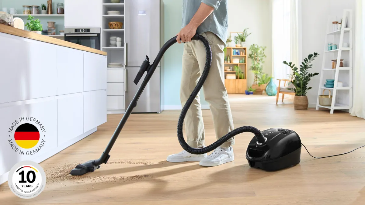 A compact, red Bosch bagged cylinder vacuum manoeuvres between two couches and a table.