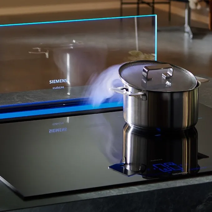 Roestvrij stalen pot op inductie kookplaat met stoom stijgen, keukenapparatuur op achtergrond.