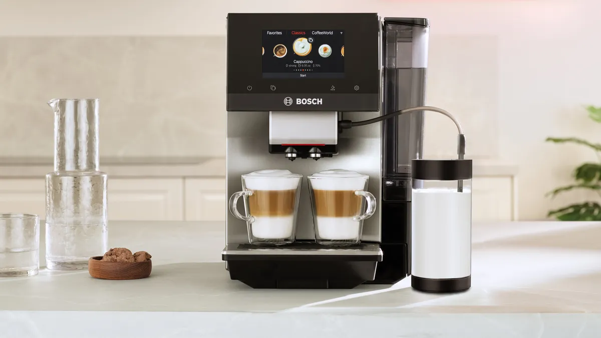 A modern Bosch coffee machine brewing two lattes, with a touchscreen display and milk container on a kitchen countertop.