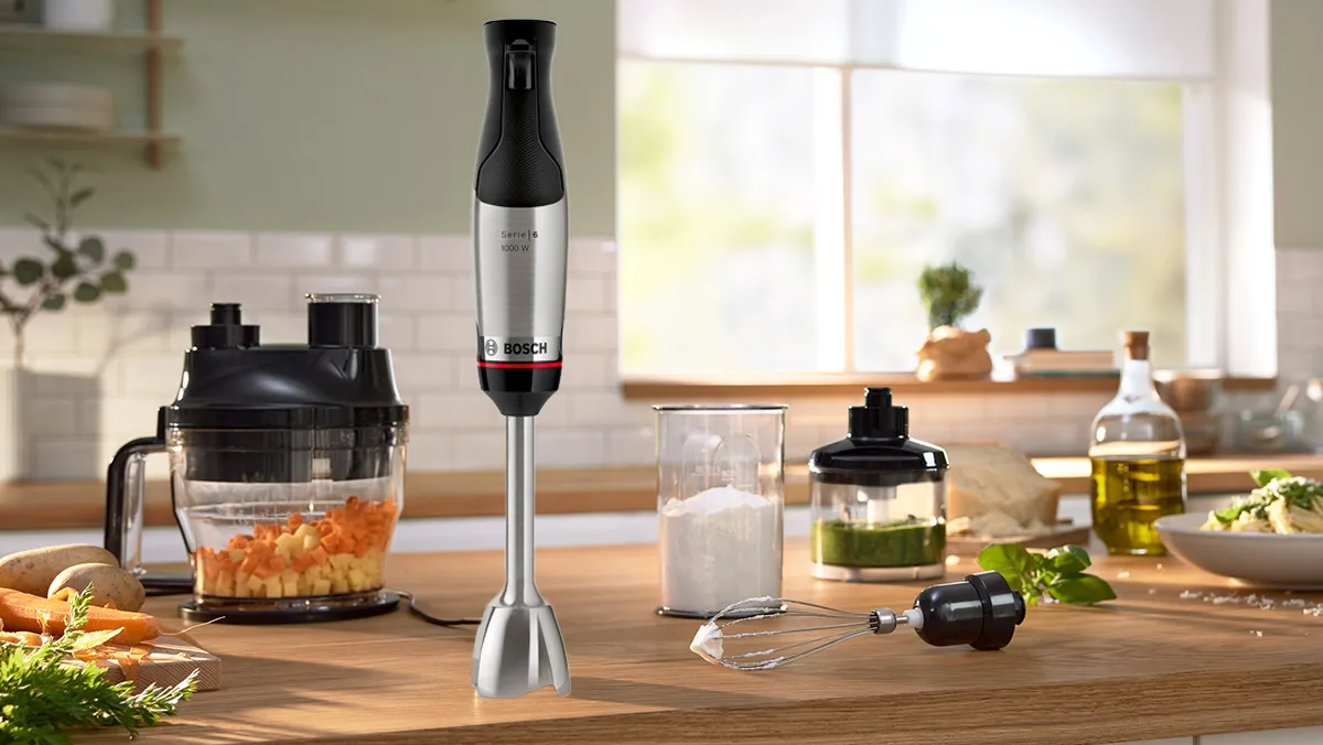 Bosch hand blender stood on kitchen counter with various attachments surrounding