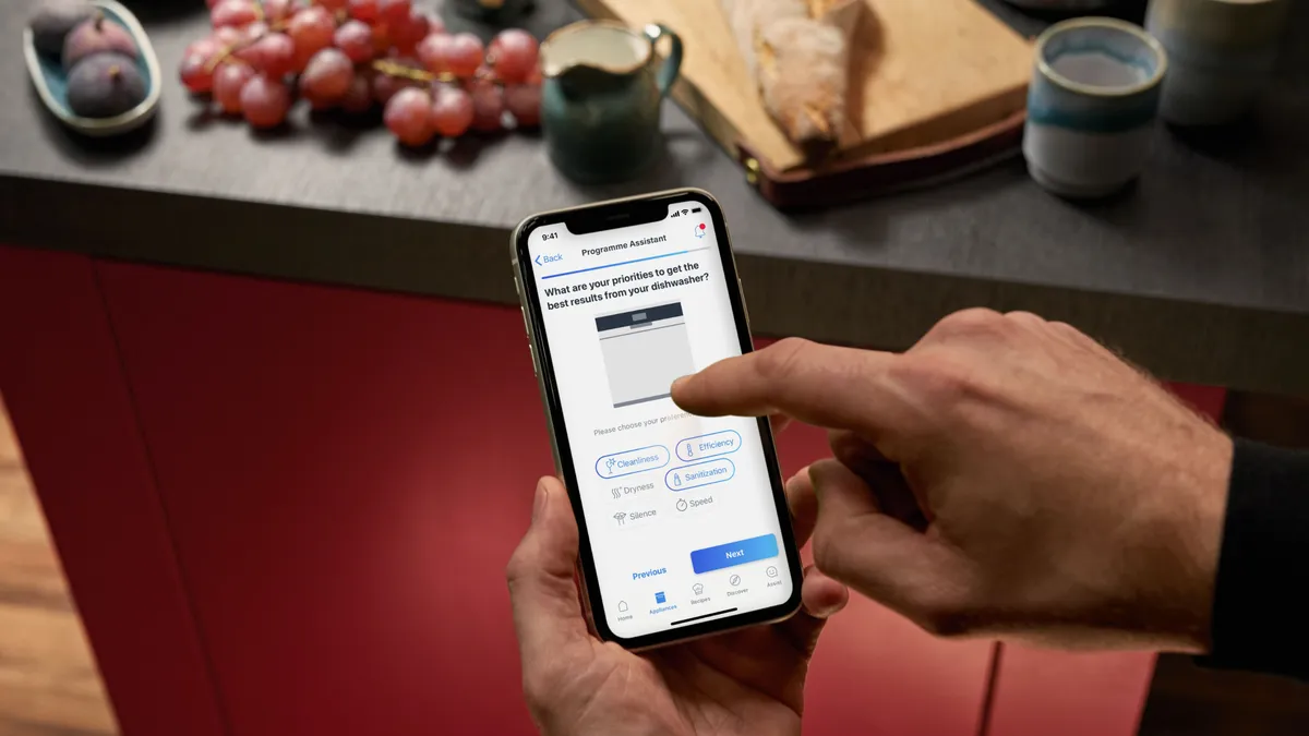 Person mit Smartphone auf Online-Banking-App auf Küchentheke mit Trauben und Brot zugreifen.