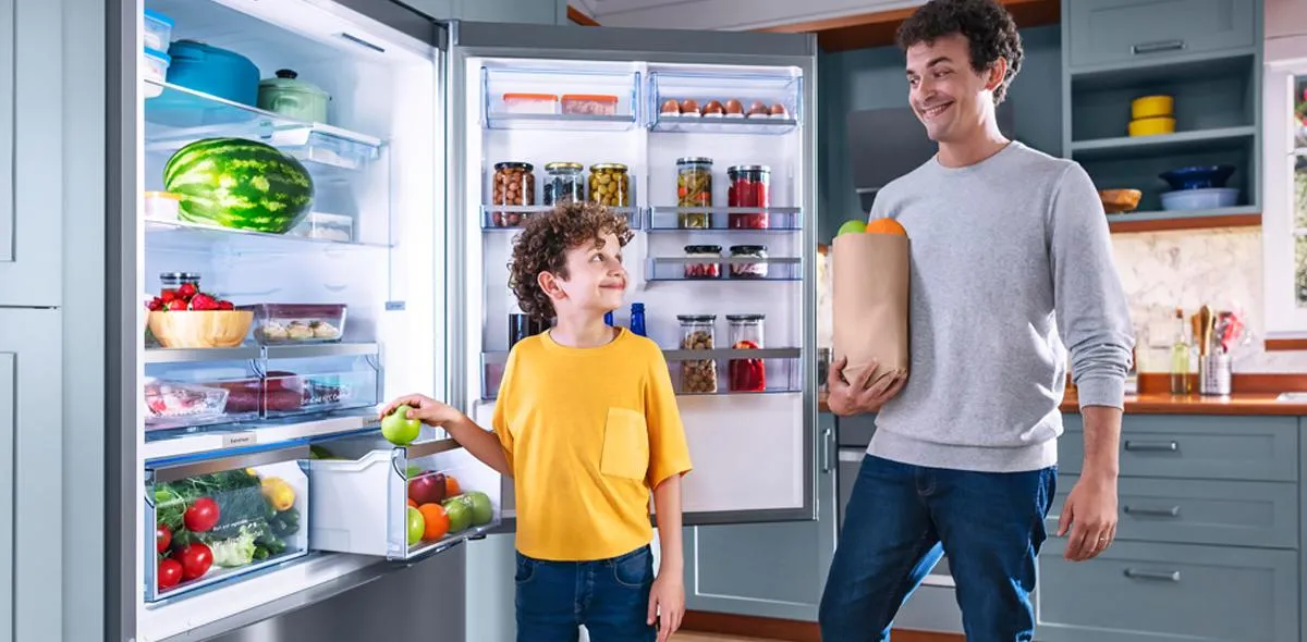 Çeşitli gıda eşyaları ile dolu açık bir buzdolabının önünde duran iki kişi.