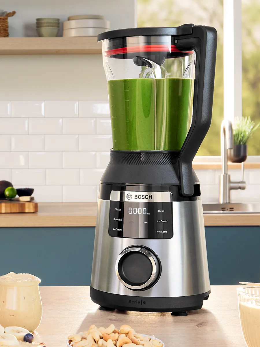 Un blender Bosch cu recipient din sticlă, plin cu smoothie verde, așezat pe blatul din bucătărie, cu panou de control digital și design elegant.
