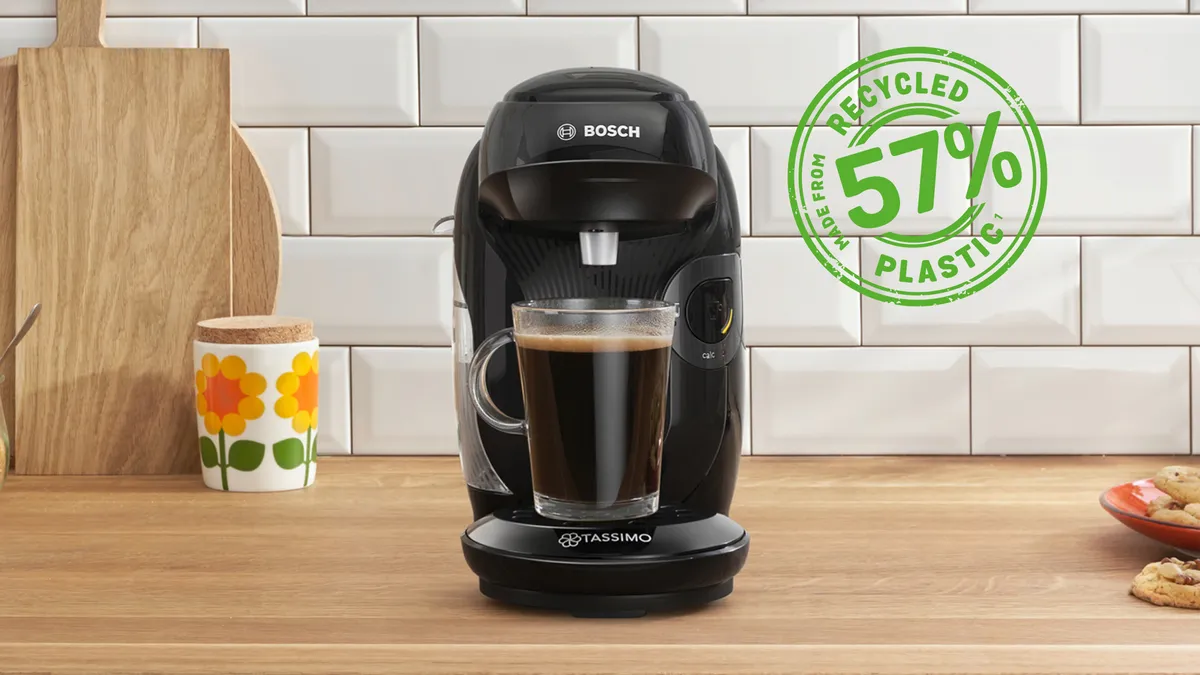 The coffee machine TASSIMO STYLE friendly on a kitchen worktop with a filled coffee cup.