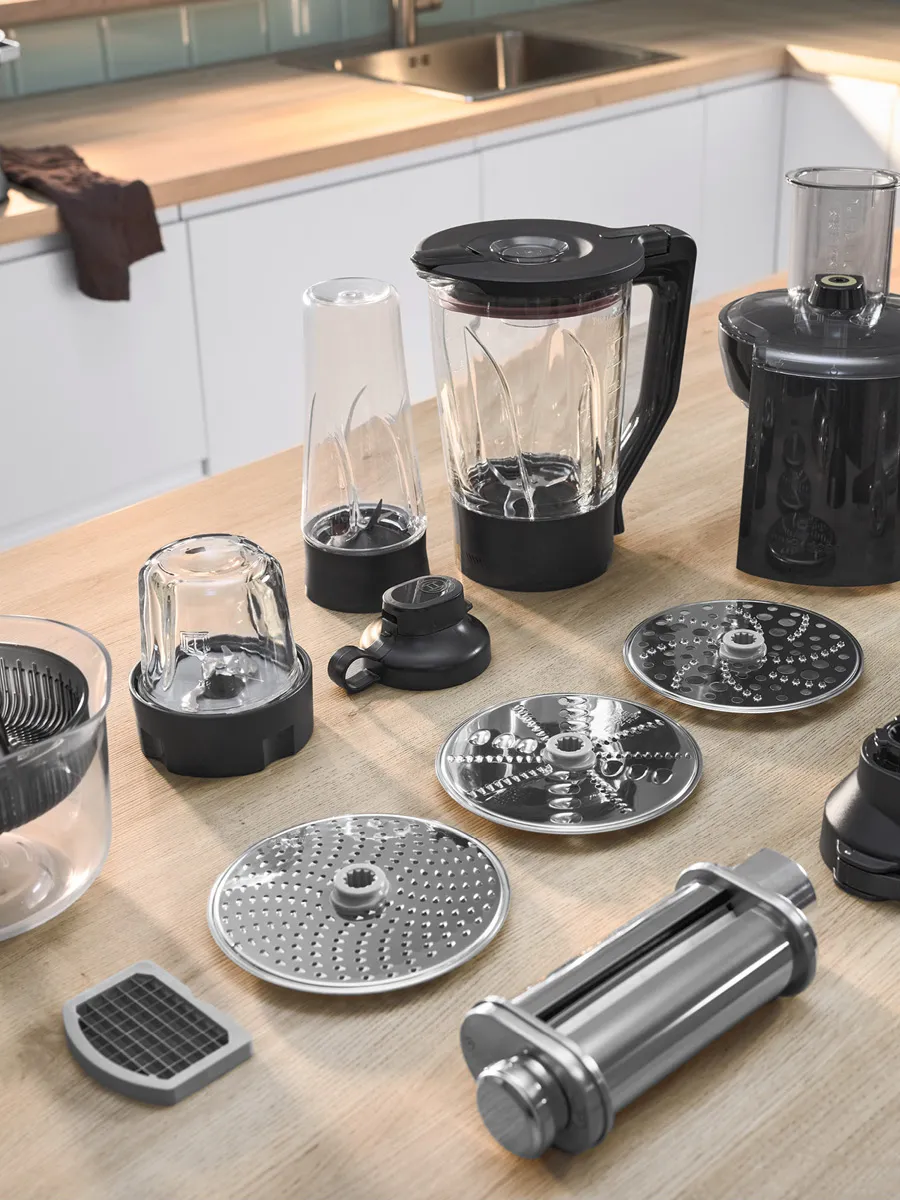 Une collection de pièces d'appareils de cuisine, y compris des récipients de mixeur, des lames et divers accessoires, disposée sur une planche en bois.