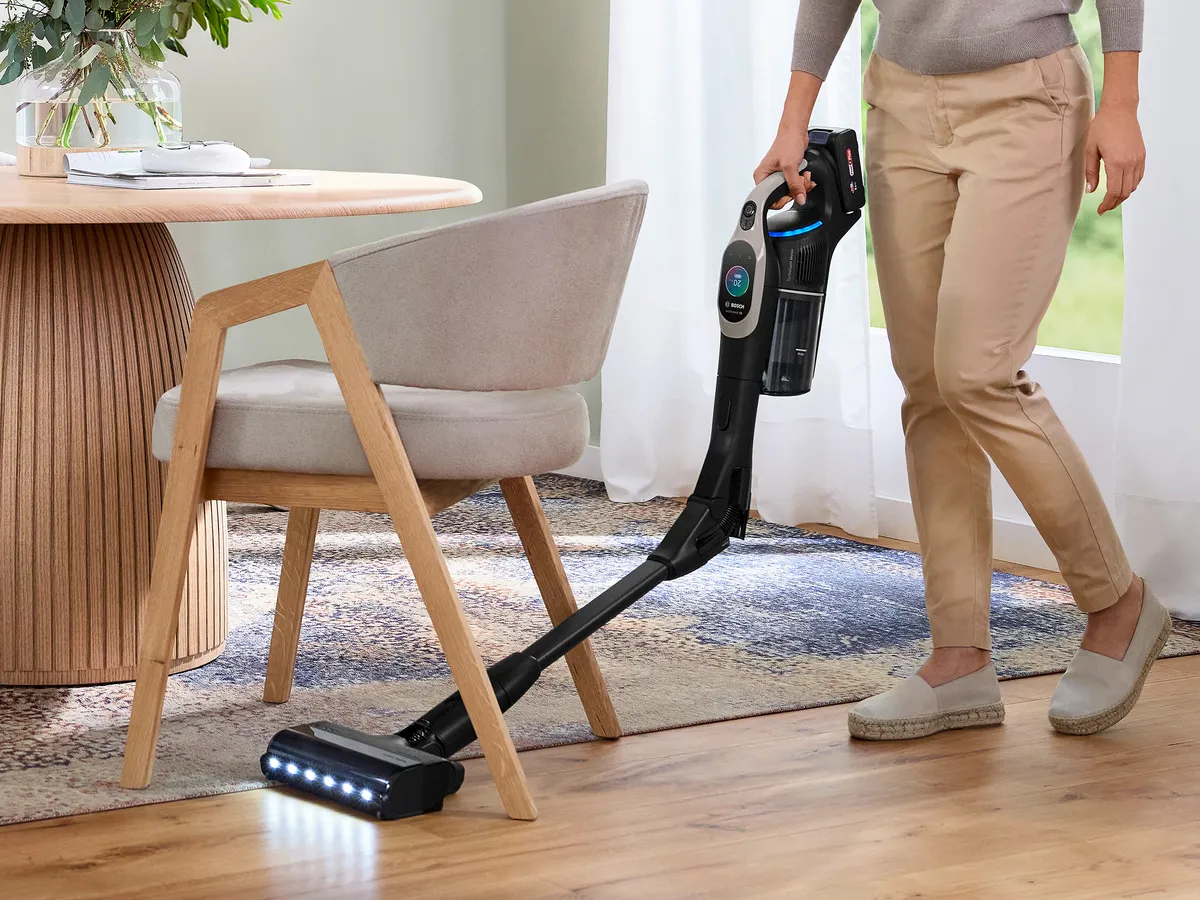 Osoba używająca bezprzewodowego odkurzacza do sprzątania pokoju ze stołem i krzesłem.