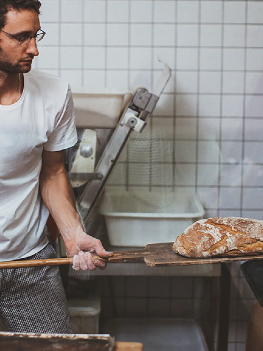 Ενας άνδρας που βγάζει το ψωμί απ΄τον φούρνο με μια ξύλινη σπάτουλα.