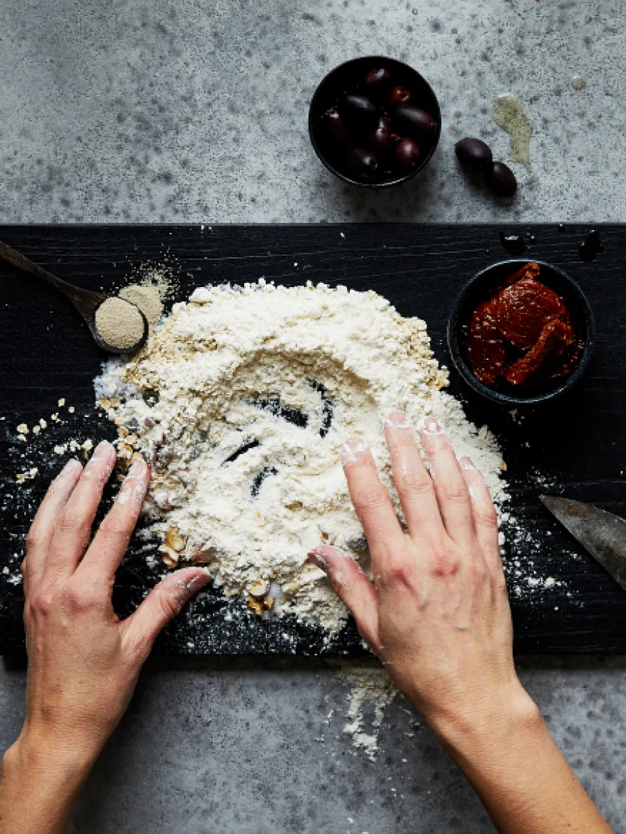 Δύο χέρια που ανακατεύουν το αλεύρι με τα υπόλοιπα υλικά.