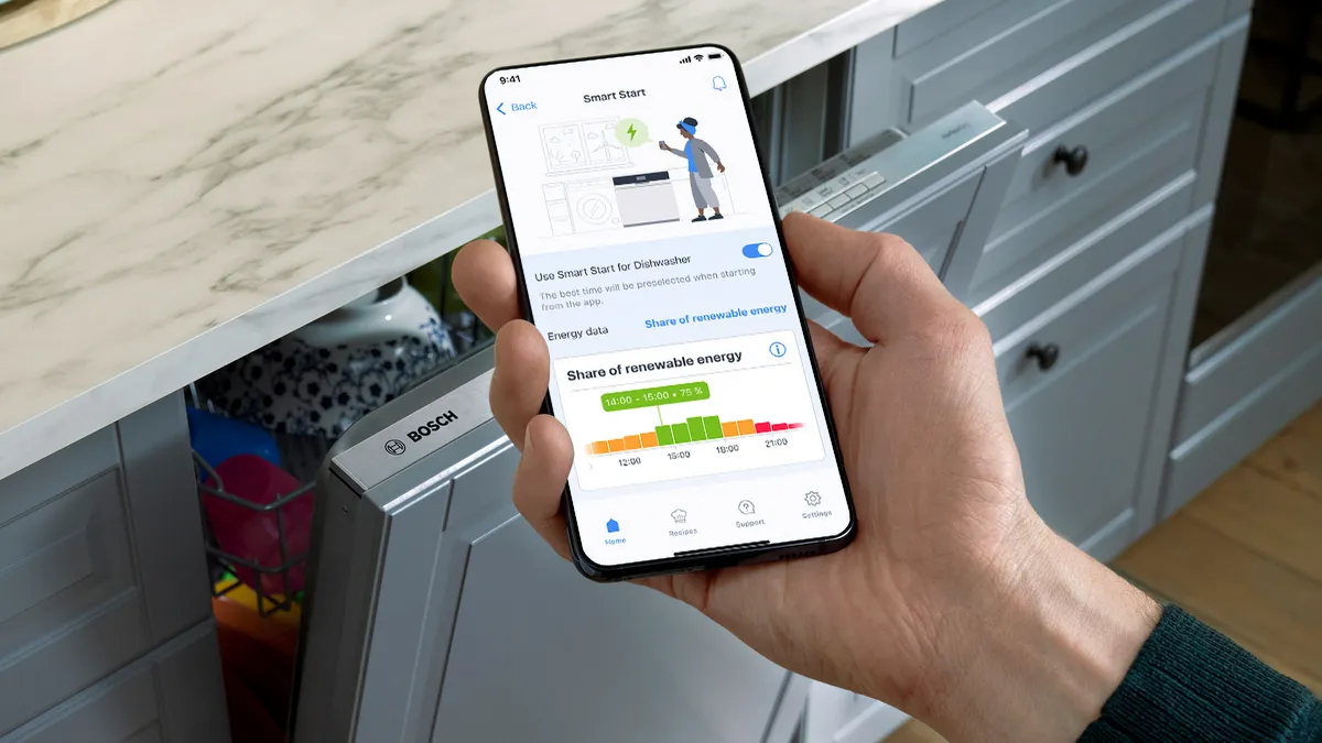 Smartphone visar energianvändningsapp, person som står bredvid apparaten i köket.