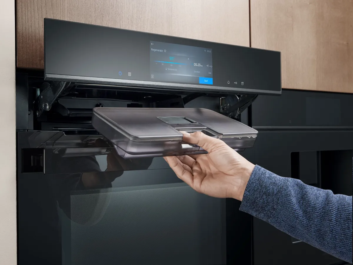 Een persoon voegt water toe aan een Siemens inbouw oven om te stomen.