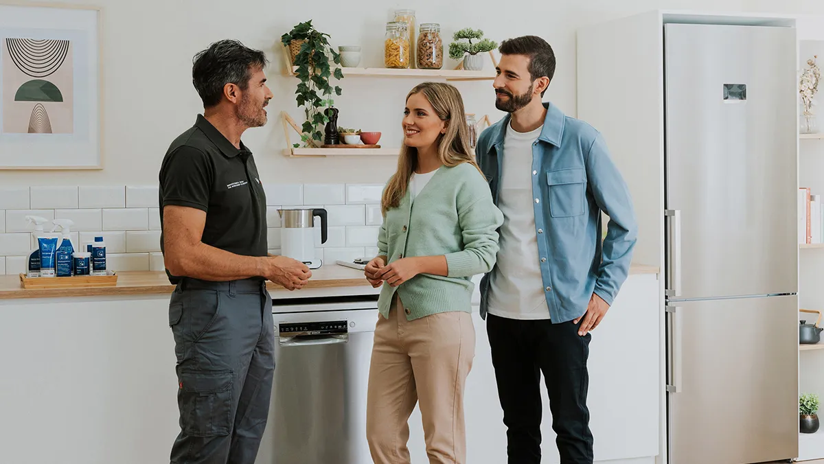 A young couple consults with a technician in a bright, modern kitchen full of Bosch appliances.