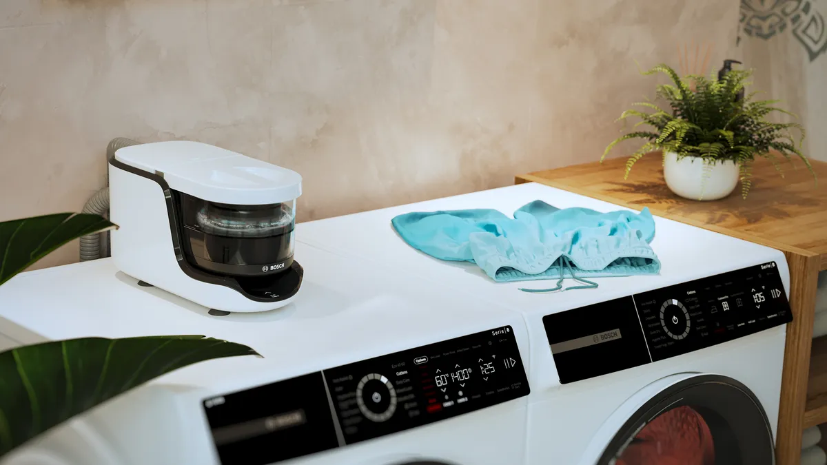 Une machine à laver Bosch moderne avec un lave-linge compact dessus, présentant du linge bleu et une plante décorative dans une salle de lavage élégante.