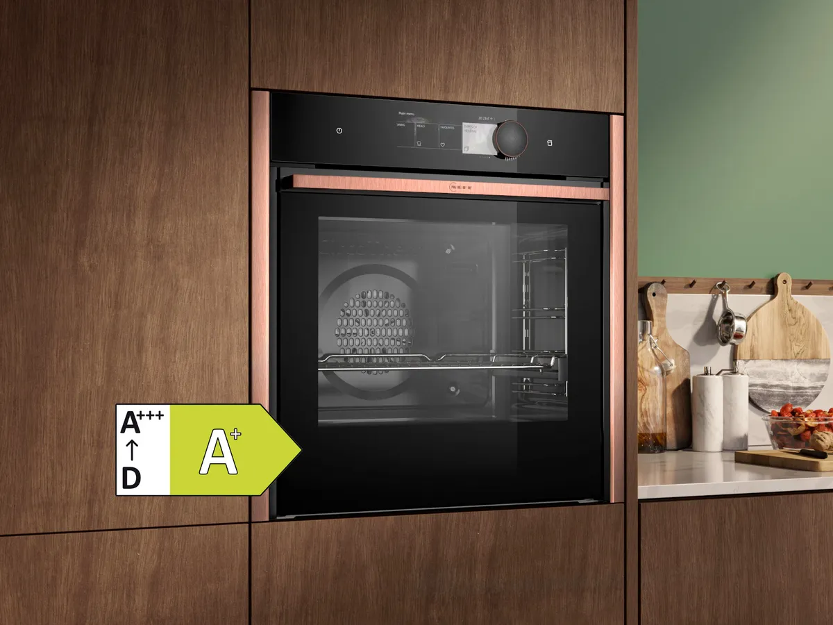 Modern oven built into wooden cabinets with black glass front and energy efficiency class A+. The kitchen equipment includes various utensils.