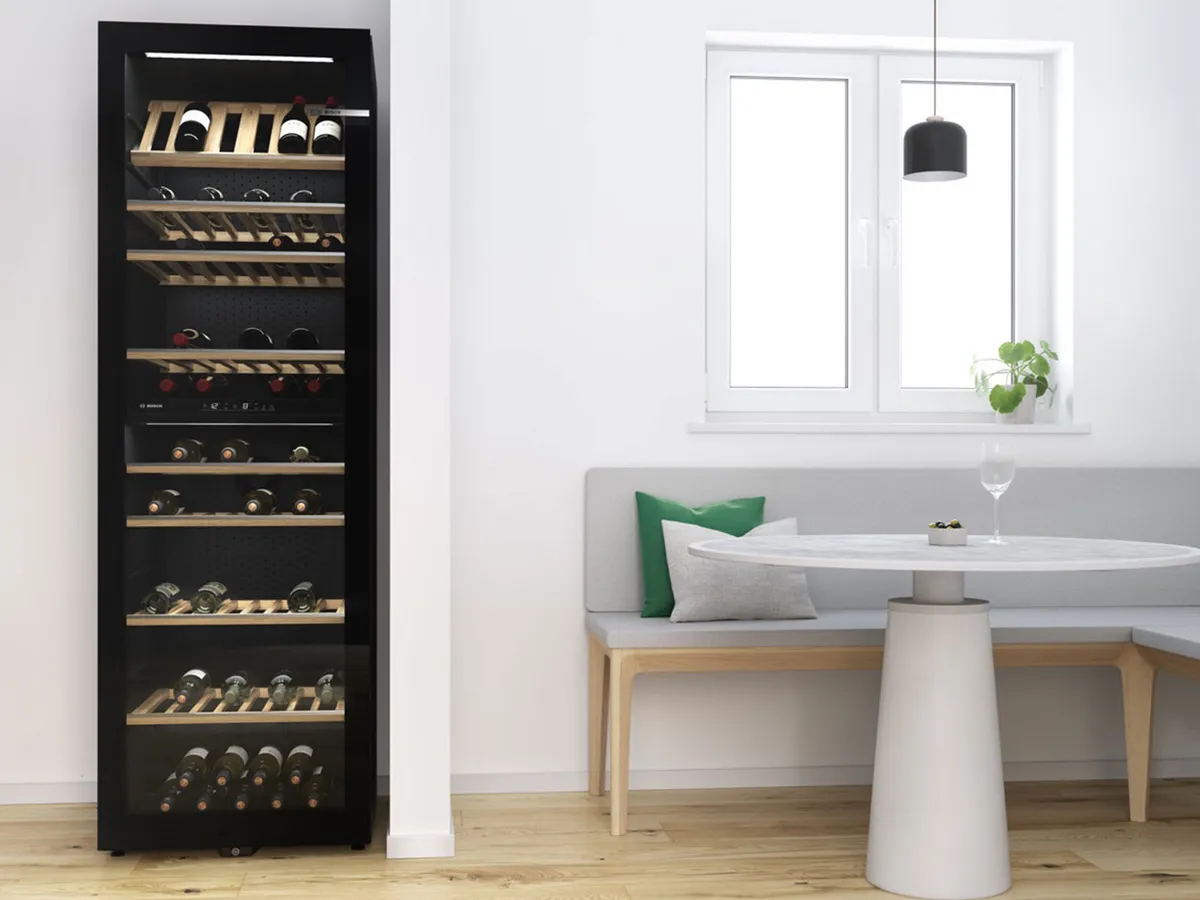 Grande cave à vin Bosch noire, vitrée et remplie, dans une cuisine moderne avec coin repas.