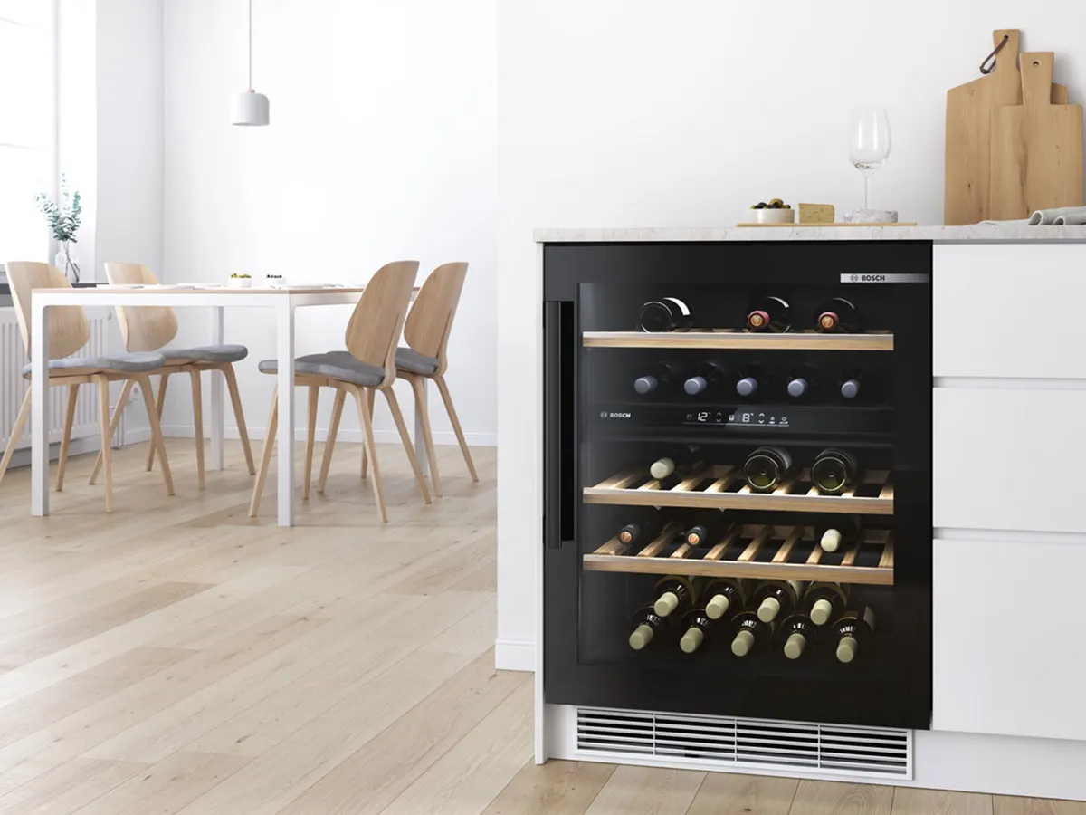 Cave à vin encastrée Bosch noire dans une cuisine moderne avec sol en bois clair et salle à manger.