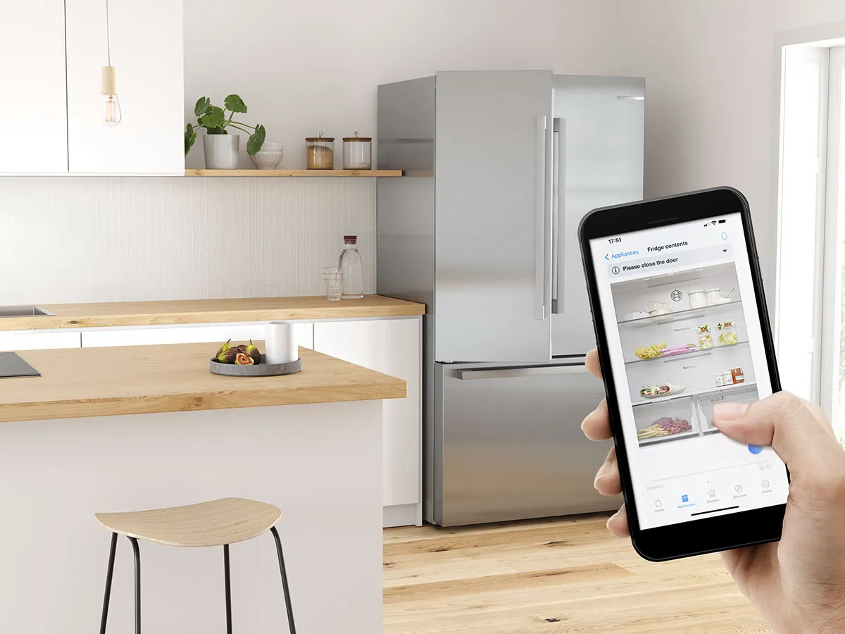 Réfrigérateur connecté Bosch contrôlé via une application sur smartphone dans une cuisine moderne.