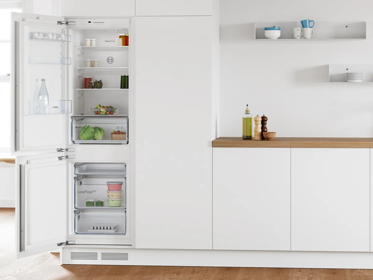 Réfrigérateur-congélateur encastré Bosch ouvert, rempli d’aliments frais dans une cuisine moderne.