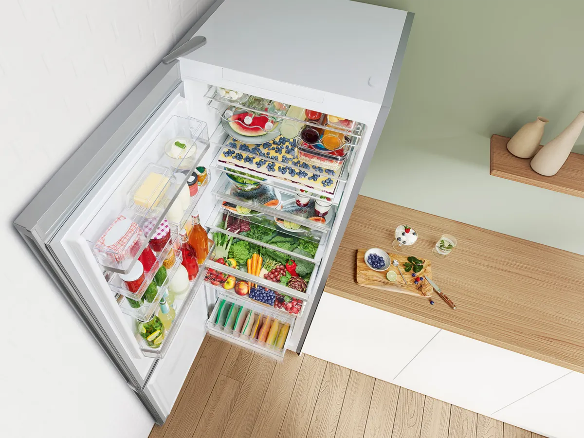 Un réfrigérateur bien organisé rempli de produits frais, de boissons et de produits laitiers, à côté d'un comptoir en bois avec des desserts et des plantes.