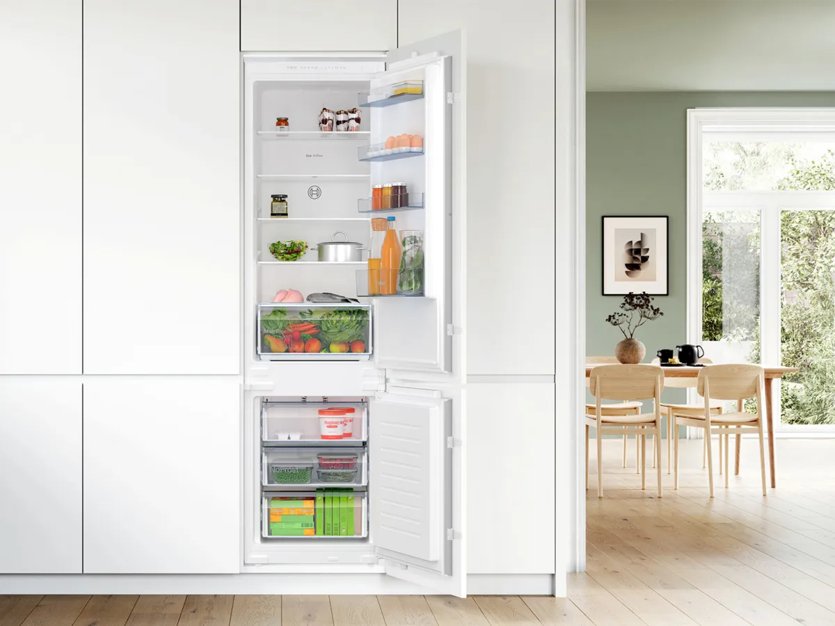 Réfrigérateur encastrable blanc ouvert, bien rempli, dans une cuisine moderne lumineuse.