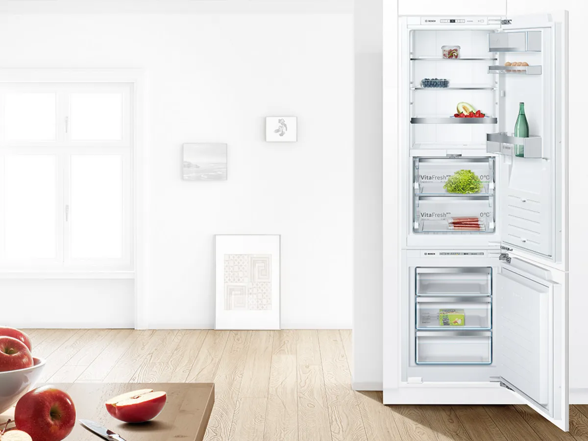 Réfrigérateur encastrable ouvert dans une cuisine blanche avec des aliments bien rangés.