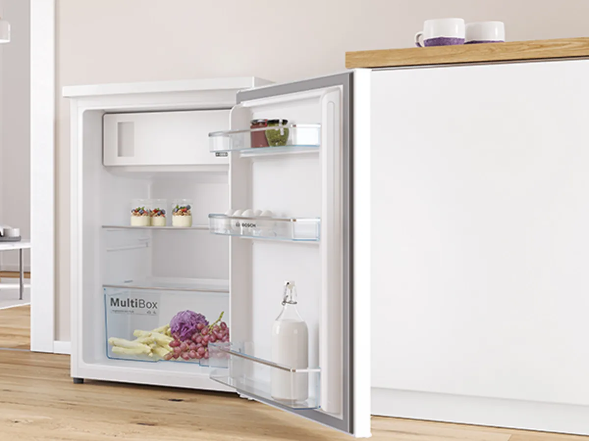 Petit réfrigérateur encastré sous un plan de travail, porte ouverte montrant des aliments frais.
