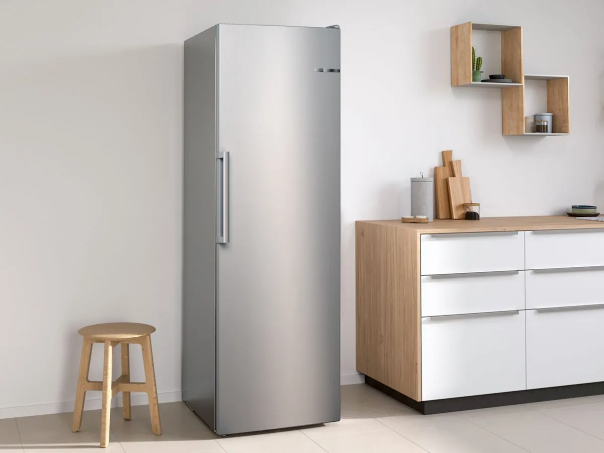 Réfrigérateur Bosch inox dans une cuisine moderne, à côté d’un tabouret en bois.