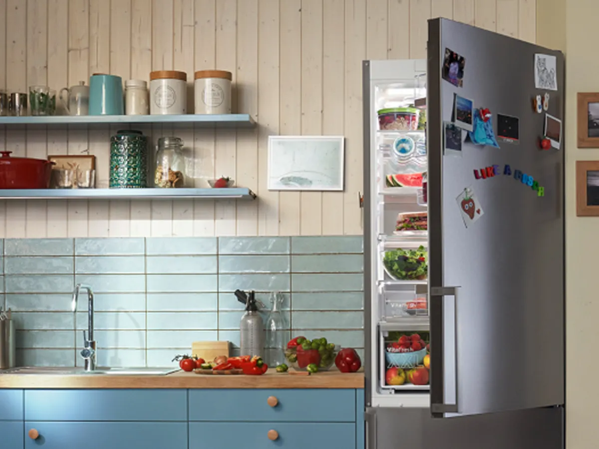 Une cuisine moderne avec un réfrigérateur en acier inoxydable ouvert pour révéler des produits frais, ainsi qu'une décoration de cuisine colorée et des étagères en bois.